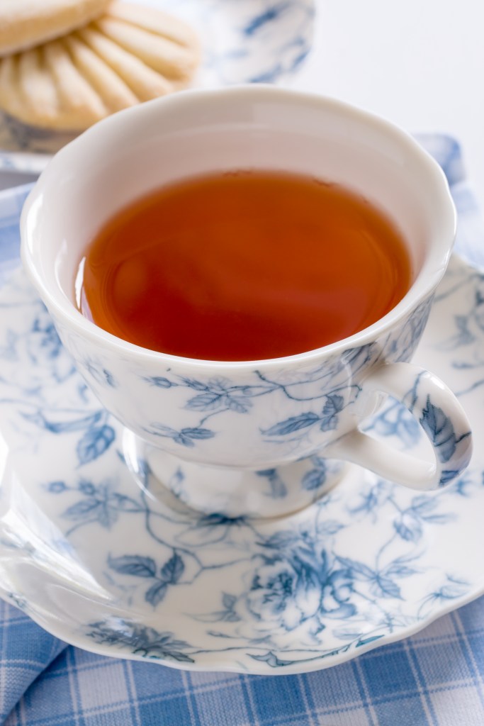 A nice cup of English tea served in traditional fine floral pattern porcelain cup and saucer with defocussed biscuits in the background